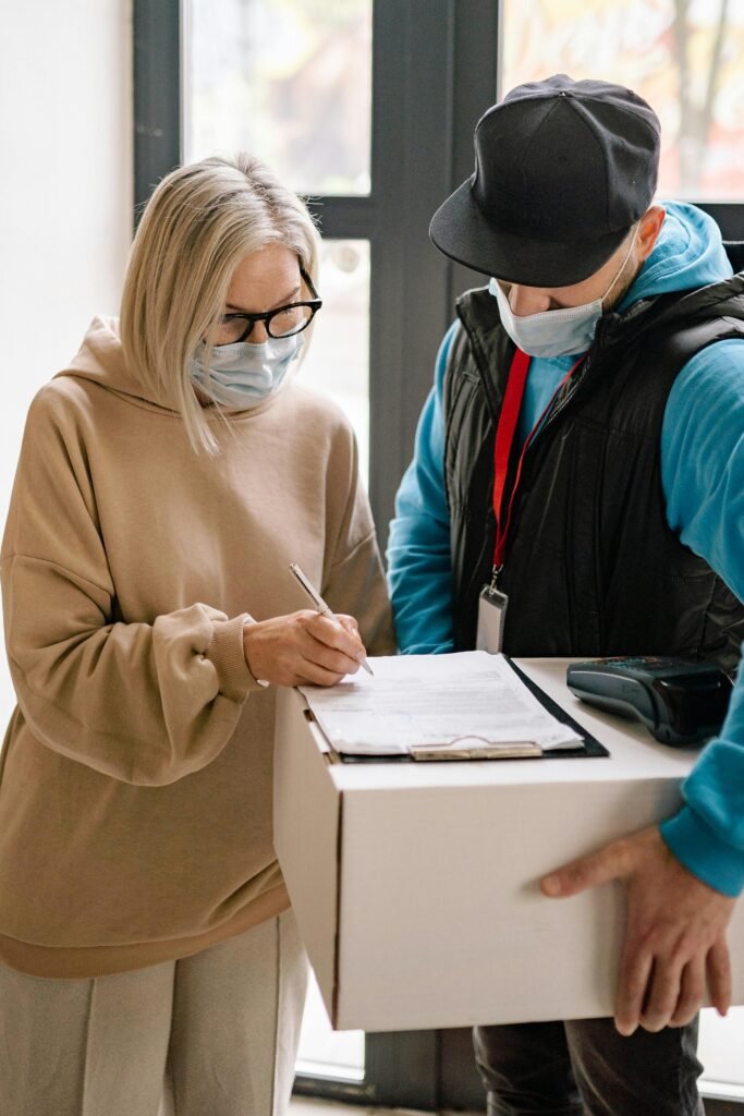 Elderly woman wearing face mask signs for a parcel delivery indoors.